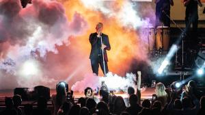 A performer stands on stage accented by smoke and a light show